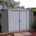 Green and white garden shed with sliding doors.
