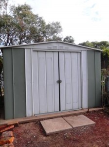 Green and white garden shed with sliding doors.