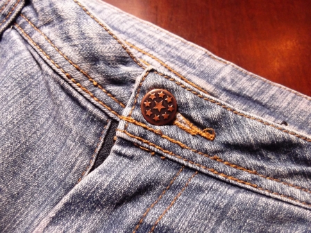 Close up of the waist of a pair of blue jeans with the brass button done up.