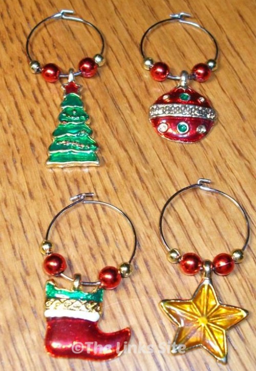 Four Christmas themed metal wine charms on a wooden table.