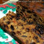 Christmas cake on a wooden cutting board. There is a Christmas serviette partially under the cake and one side of the cake has been sliced. Text overlay says: Easy Mix Christmas Cake! (best Christmas cake recipe I've ever tried!).