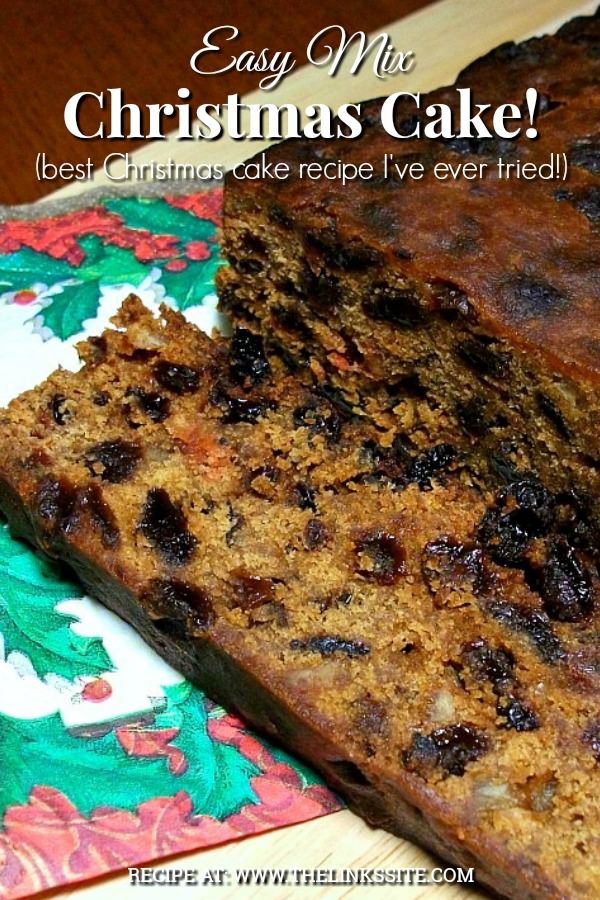Christmas cake on a wooden cutting board. There is a Christmas serviette partially under the cake and one side of the cake has been sliced. Text overlay says: Easy Mix Christmas Cake! (best Christmas cake recipe I've ever tried!).