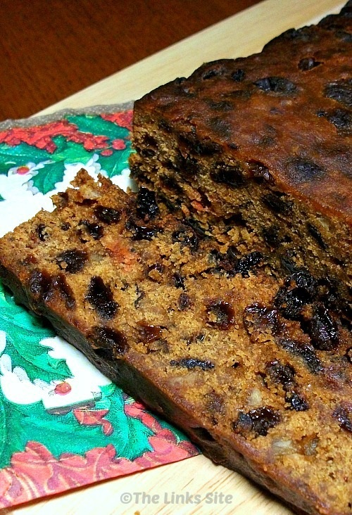 Christmas cake on a wooden cutting board. There is a Christmas serviette partially under the cake and one side of the cake has been sliced.