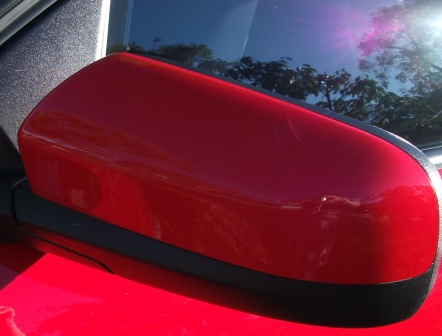 Red car side mirror that is clean and free from bugs.
