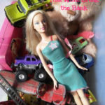 Overhead view of a box of children's toys containing toy cars, a Barbie, and a teddy. Text overlay reads: Easy Activities for Kids, That Won't Break the Bank.