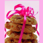 A stack of four chocolate chip cookies with a pink and white background. The cookies are loosely wrapped with pink decorative curling ribbon and there is a bunch of curled ribbon on top of the cookies. Text overlay says: Oh So Easy Chocolate Chip Cookies.