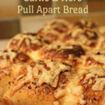 Cheesy garlic and herb pull apart bread loaf on a black cooling rack. A brown and green tiled splashback is seen in the background. Text overlay says: Cheesy Garlic & Herb Pull Apart Bread.