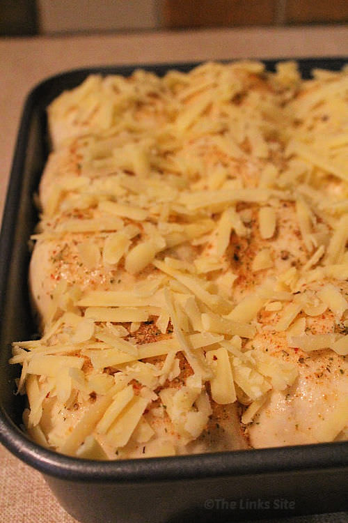 Uncooked pull apart bread dough in a baking dish, topped with garlic and herb seasoning as well as grated cheese.