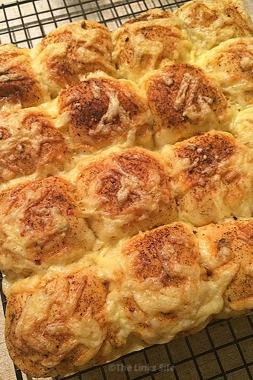 Overhead view of freshly baked cheesy garlic and herb pull apart bread on a black cooking rack.