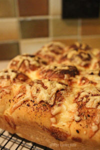 Cheesy garlic and herb pull apart bread loaf on a black cooling rack. A brown and green tiled splashback is seen in the background.
