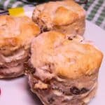 Three scones on a white plate with more scones in the background.
