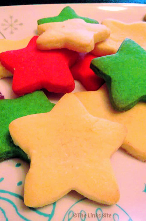 Several star shaped cookies on a white plate with a Christmas pattern. The cookies are coloured red, green, and white.