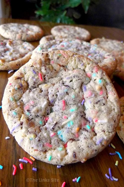 One cookie in the front is tilted up so that it is facing the camera. There are several other cookies arranged in the background and multi-coloured sprinkles scattered around the cookies.