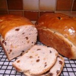 2 Freshly baked fruit loaves on a baking rack. One loaf has been partially sliced.