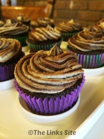 Choc orange cupcakes are pictured on white cupcake tray. Each cupcake is topped with a swirl of marbled frosting.