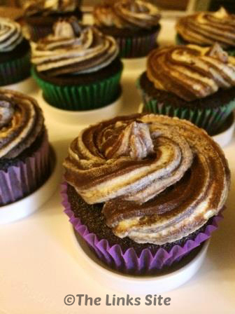 Choc orange cupcakes are pictured on white cupcake tray. The cupcakes are topped with a swirl of marbled frosting.