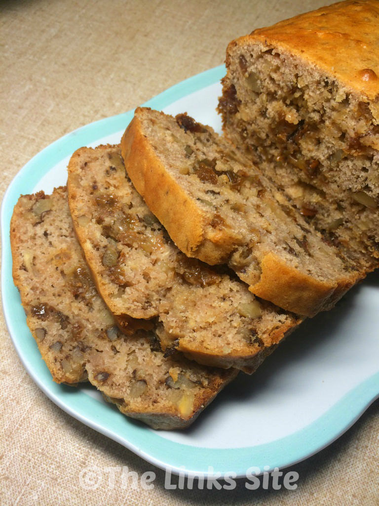 Slices of walnut raisin loaf as well as some uncut loaf on a blue and white plate.