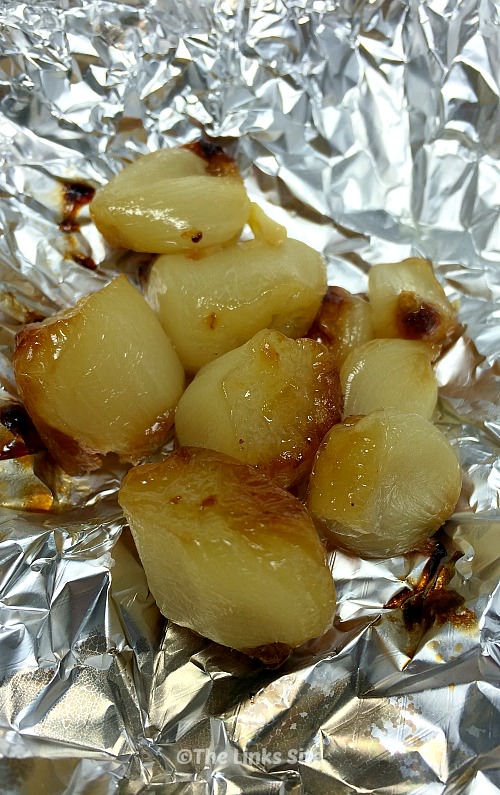 Several cloves of roasted garlic are placed on a piece of crumpled aluminium foil.