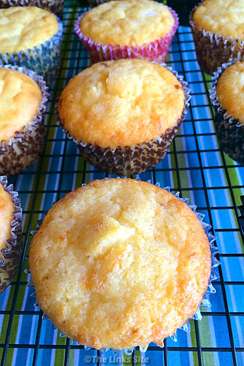 Close up overhead shot of a lemon muffin on a cooling rack surrounded by more lemon muffins. A blue and green striped tablecloth is underneath the cooling rack.