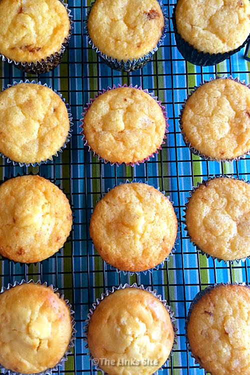 Overhead shot of 12 lemon muffins on a cooling rack. The cooling rack is on a blue and green striped tablecloth.