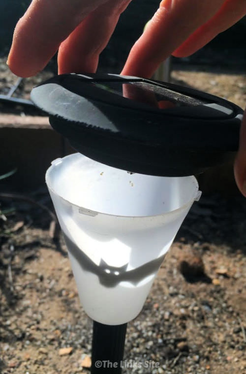 Image showing a solar light that has been decorated with a bat picture. A hand is placing the top of the light casing back on.