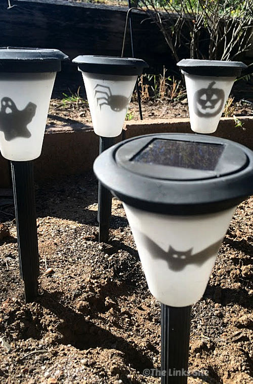 Daytime image showing a group of solar lights in a garden bed. The lights have been decorated with Halloween theme pictures.
