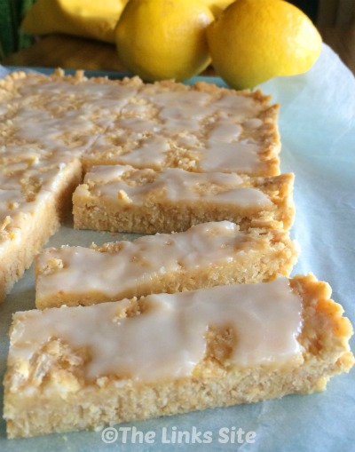 Small pieces of slice are pictured on a piece of baking paper with some whole lemons in the background.