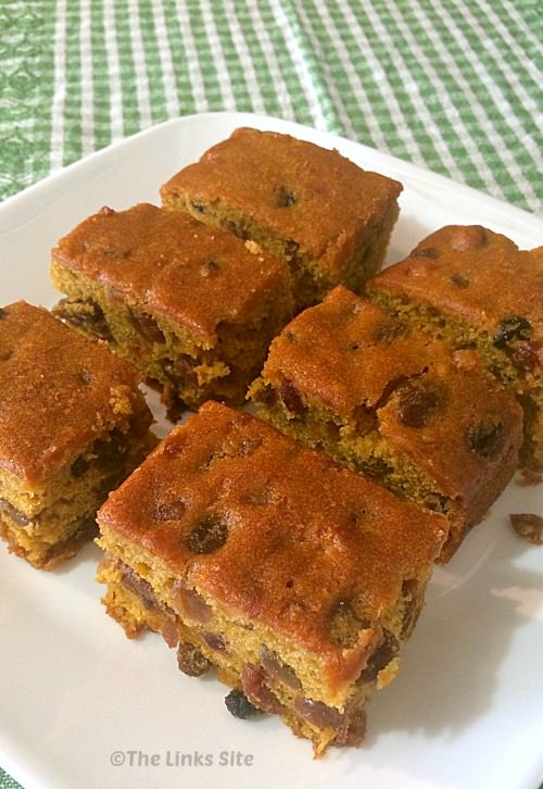 Overhead view of pieces of pumpkin fruit cake on a white plate. The white plate is sitting on a green and white check tea towel.