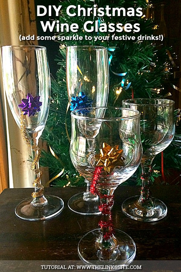 Four decorated wine glasses on a wooden table with a Christmas tree in the background. Text overlay says: DIY Christmas Wine Glasses (add some sparkle to your festive drinks!).