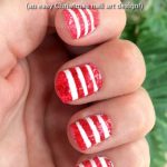 Partially closed hand showing red and white stripy fingernails. Plants can be seen in the background. Text overlay says: Cute Stripy Christmas Nails (an easy Christmas nail art design!).