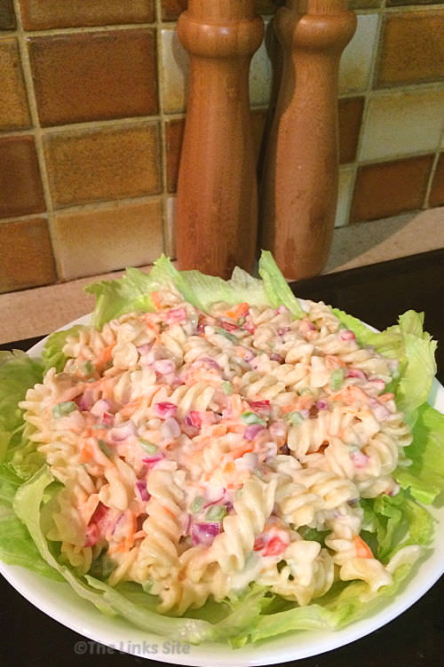 Creamy pasta salad on a bed of lettuce served in a white bowl. Wooden salt and pepper grinders can be seen in the background.