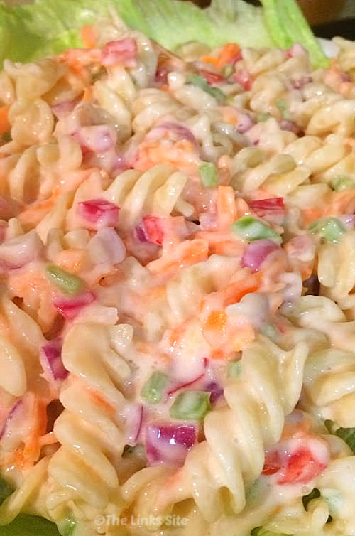 Close up of creamy pasta salad on a bed of lettuce showing spiral pasta, chopped onion, carrot, capsicum, and a creamy sauce.
