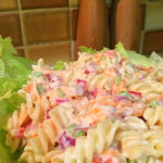 Creamy pasta salad on a bed of lettuce with wooden salt and pepper grinders in the background.