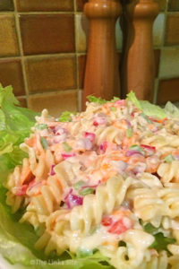 Creamy pasta salad on a bed of lettuce with wooden salt and pepper grinders in the background.