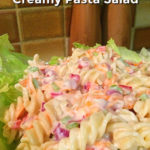 Creamy pasta salad on a bed of lettuce with wooden salt and pepper grinders in the background. Text overlay says: Delicious Homemade Creamy Pasta Salad.