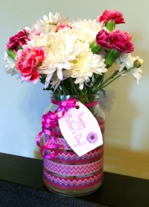 Vase made from a clear glass jar that has been decorated with washi tape in shades of pink and purple. The vase is filled with white chrysanthemums and pink carnations. A small ‘Happy Mother’s Day’ gift tag is attached with pink curling ribbon.