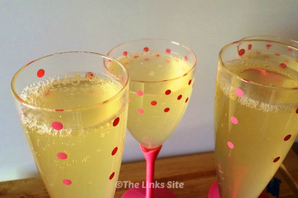 3 Plastic glasses that contain bubbly mock champagne. The top of the glasses are clear with pink spots.