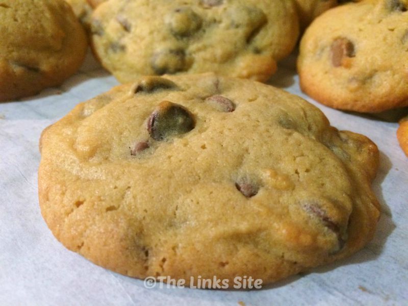 One cookie resting on baking paper is in the foreground and more cookies can be seen in the background.