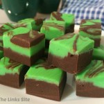 Squares of green and brown fudge on a white plate. Dark green coffee mugs and a blue and white check tea towel can be seen in the background.