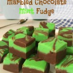 Squares of green and brown fudge on a white plate. A spoon, two dark green coffee mugs, and a blue and white check tea towel can be seen in the background. Text overlays says: Marbled Chocolate Mint Fudge.