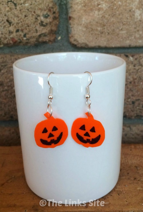A pair of orange Jack O Lantern earrings hanging from a white mug. 
