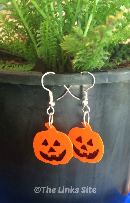 A pair of orange Jack O Lantern earrings hanging on a black plant pot.