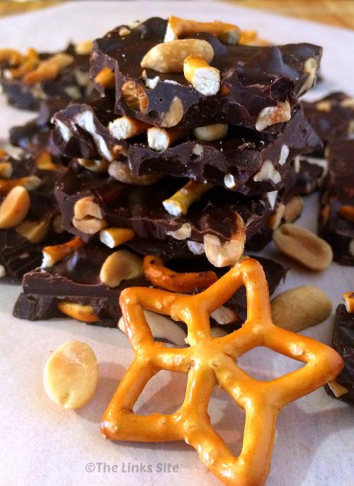 Pieces of chocolate bark stacked one on top of each other. A star shaped mini pretzel is placed in front of the bark.