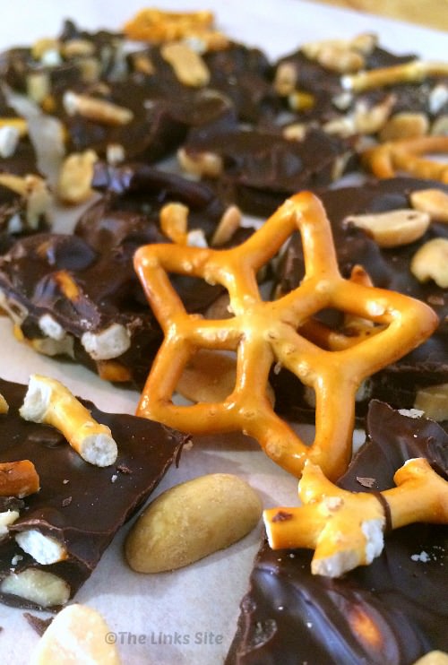 Pieces of chocolate bark sitting on baking paper. Peanuts are scattered around and a star shaped mini pretzel is place in the middle of the image.