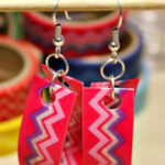 Two earrings decorated with pink, purple, and white zig zag patterned washi tape are pictured hanging from a wooden skewer. Text overlay says: Quick & Easy Washi Tape Earrings.