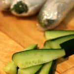Fresh cucumber sticks on a chopping board with wrapped cucumbers in the background, showing the results of proper storage.