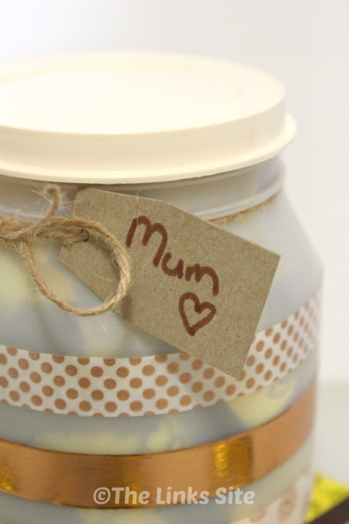 Close up of a cardboard gift tag that is addressed to Mum and attached to the neck of the plastic container with twine.