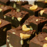 Squares of dark chocolate fudge containing pieces of peanuts lined up in rows on baking paper. Text overlay says: Easy Nutty Microwave Fudge (only 4 ingredients!).