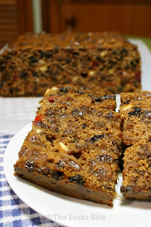 Slices of fruit cake on a plate with the remaining uncut cake in the background.