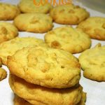 Stack of three cookies on baking paper, more cookies can be seen in the background. Text overlay says: Golden Cornflake Cookies.